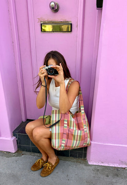 Mujer sentada con tote bag tartán rosa al hombro frente a puerta lila